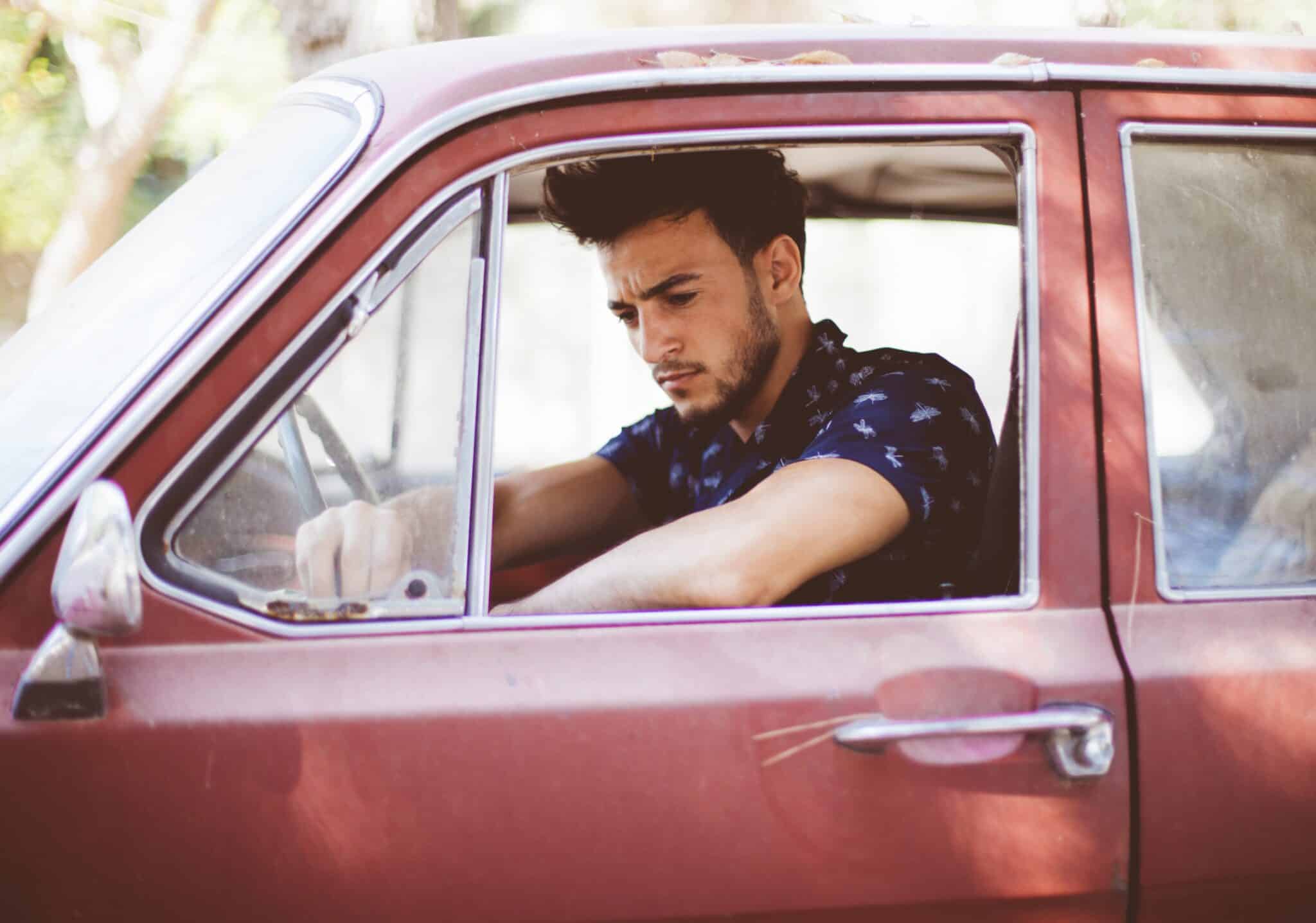 Jeune conducteur à bord de sa première voiture d'occasion rouge